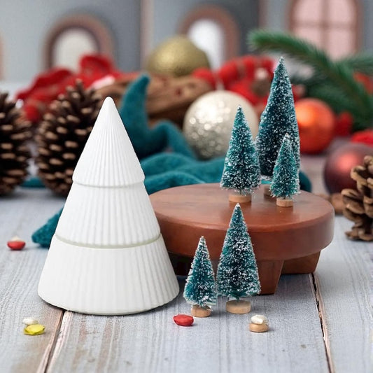 White ceramic Christmas tree with small decorative trees and ornaments on a wooden surface.
